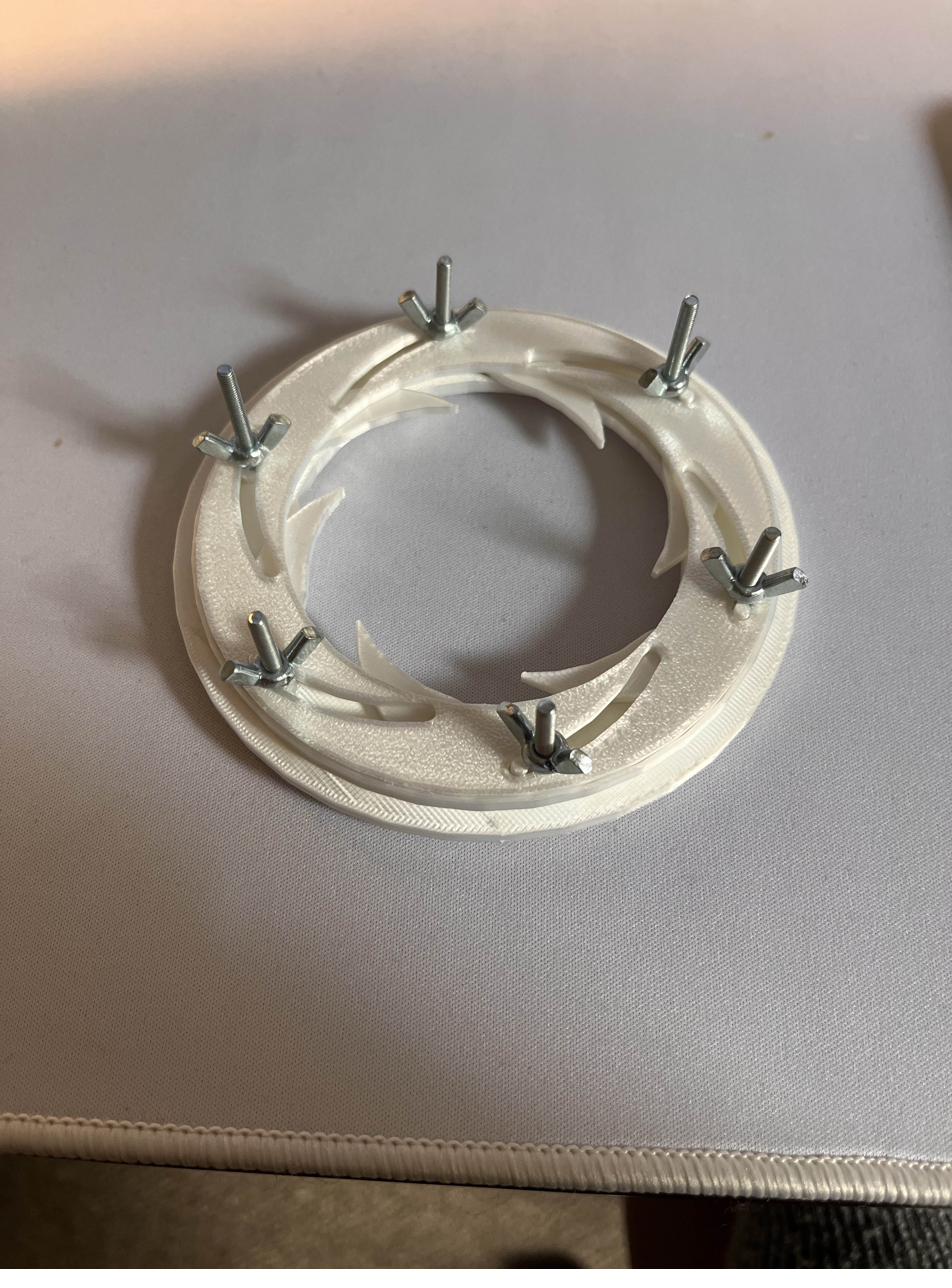 Early 3D printed iris ring with six blade pins, lying flat on a desk.