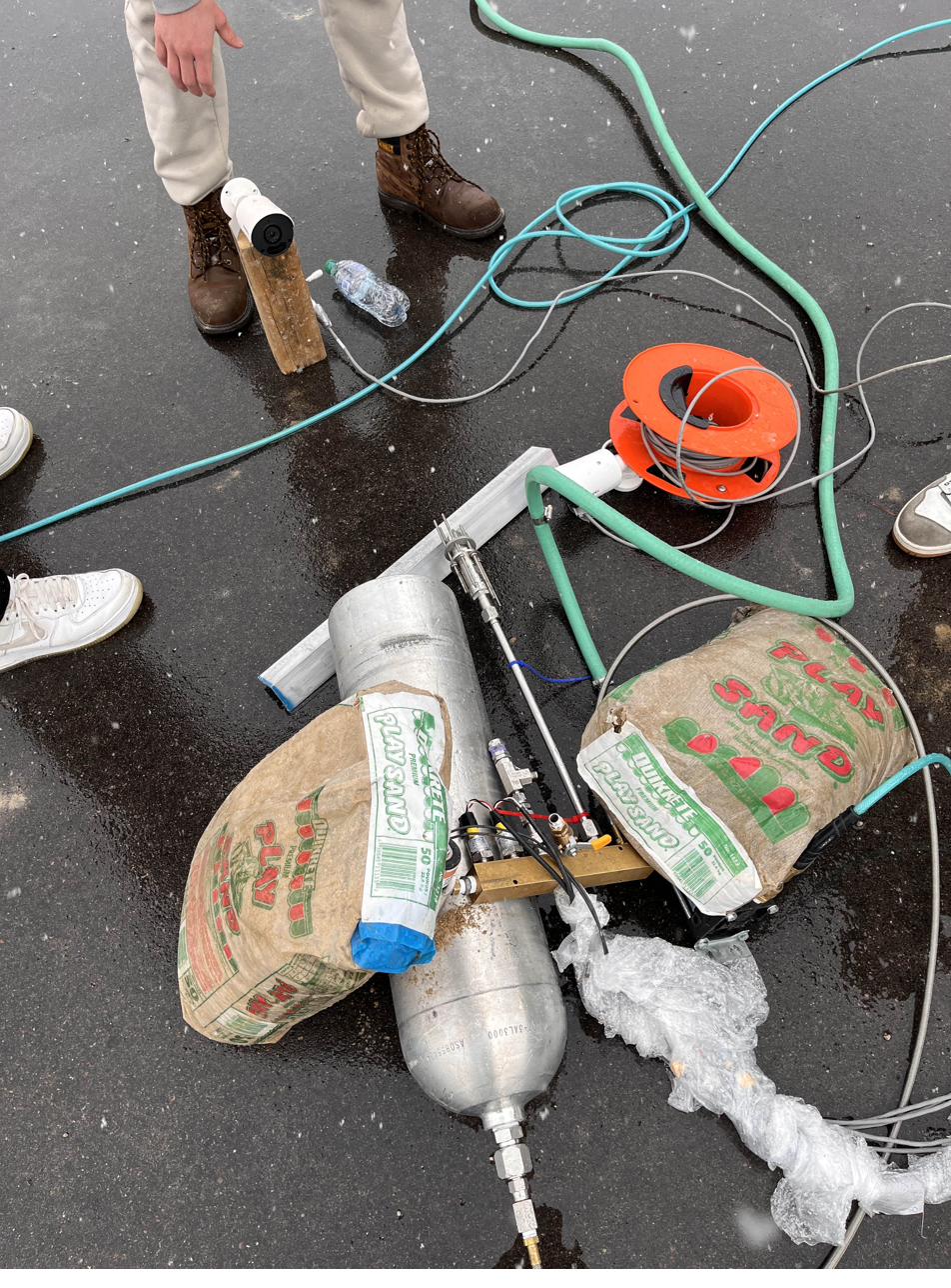 Hydrostatic proof test setup outdoors: the valve and QD plumbed in, ballasted with sandbags on the pavement, with the test lead standing beside it.