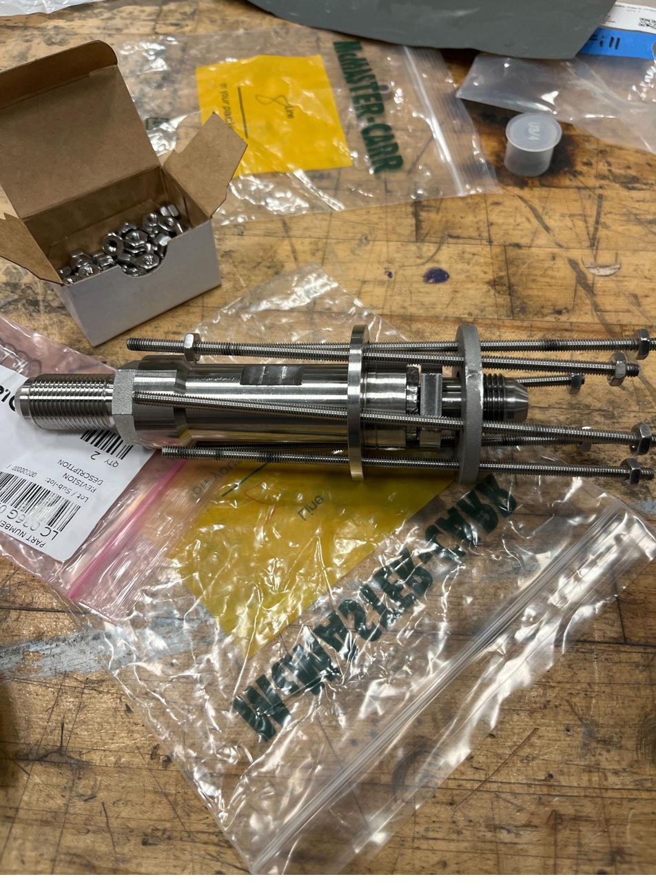 The finished stainless steel valve and QD assembly on a workbench, with the O-rings and fasteners laid out beside it.